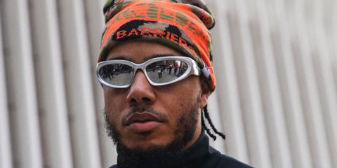 Rapper and record producer AJ Tracey was seen wearing grey silver Balenciaga BB0157S 004 wraparound sunglasses.