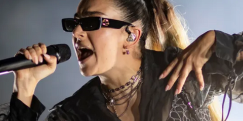 Charli XCX performing on stage and wearing Gucci rectangular sunglasses with gold interlocking GG logo.