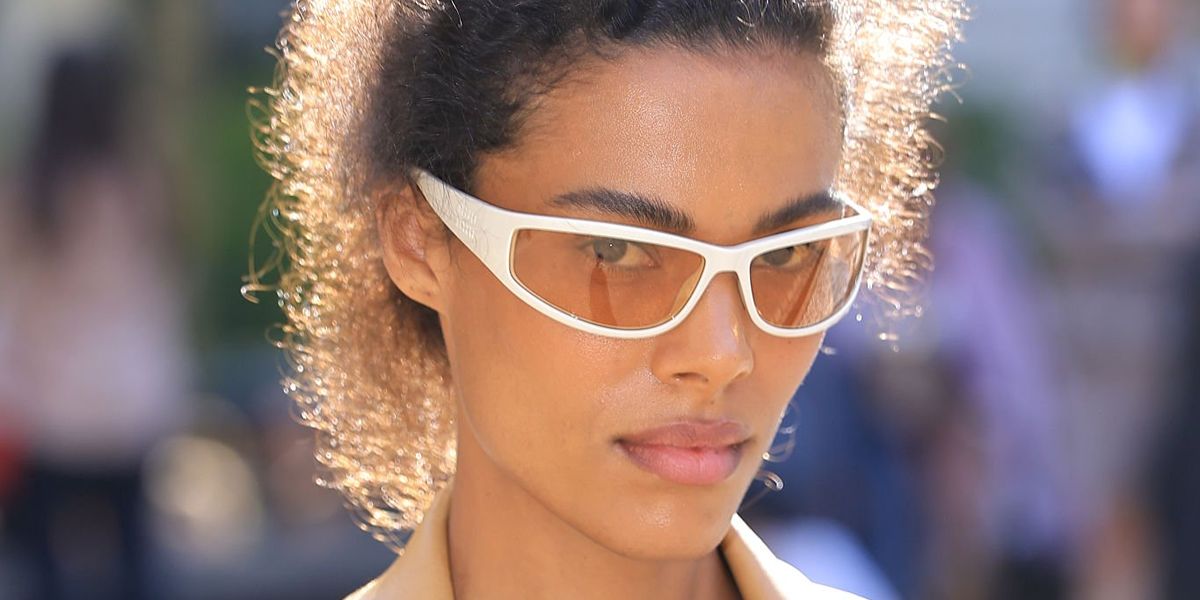 Tina Kunakey wore white Miu Miu MU C06SU 21D90X wraparound sunglasses with orange lenses at the Miu Miu Spring Summer 2027 show during Paris Fashion Week.